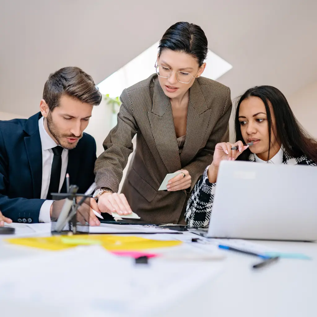 A woman points to a document on a table, with another man and a woman looking at it.