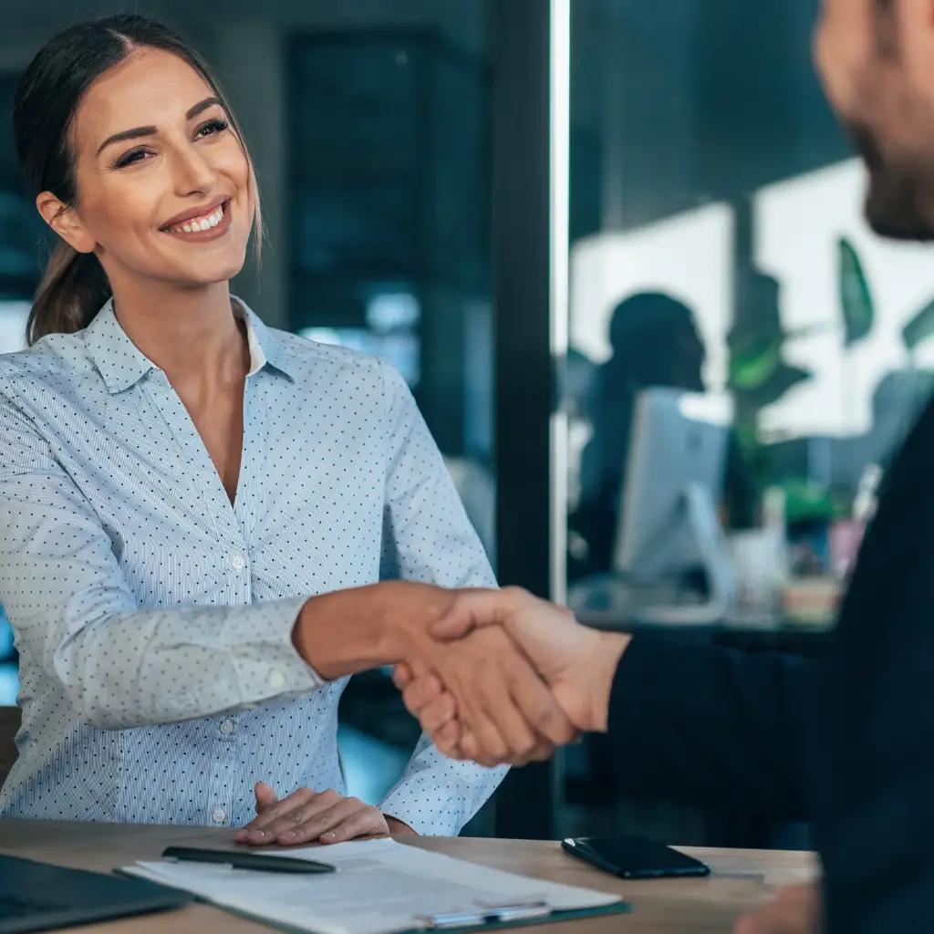 Woman smiling and shaking hands with a man in a suit.